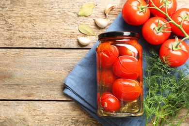 Tasty pickled tomatoes in jar, spices and fresh vegetables on wooden table, top view. Space for text