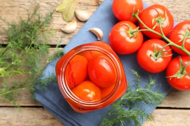 Tasty pickled tomatoes in jar, spices and fresh vegetables on wooden table, top view