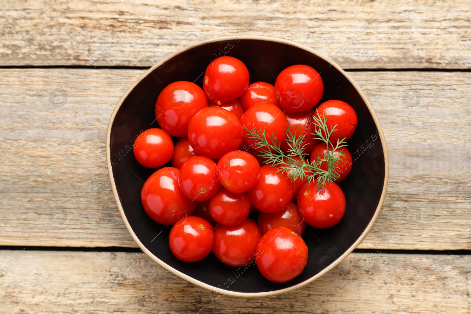 Photo of Tasty pickled tomatoes and dill in bowl on wooden table, top view