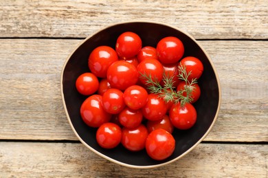 Photo of Tasty pickled tomatoes and dill in bowl on wooden table, top view