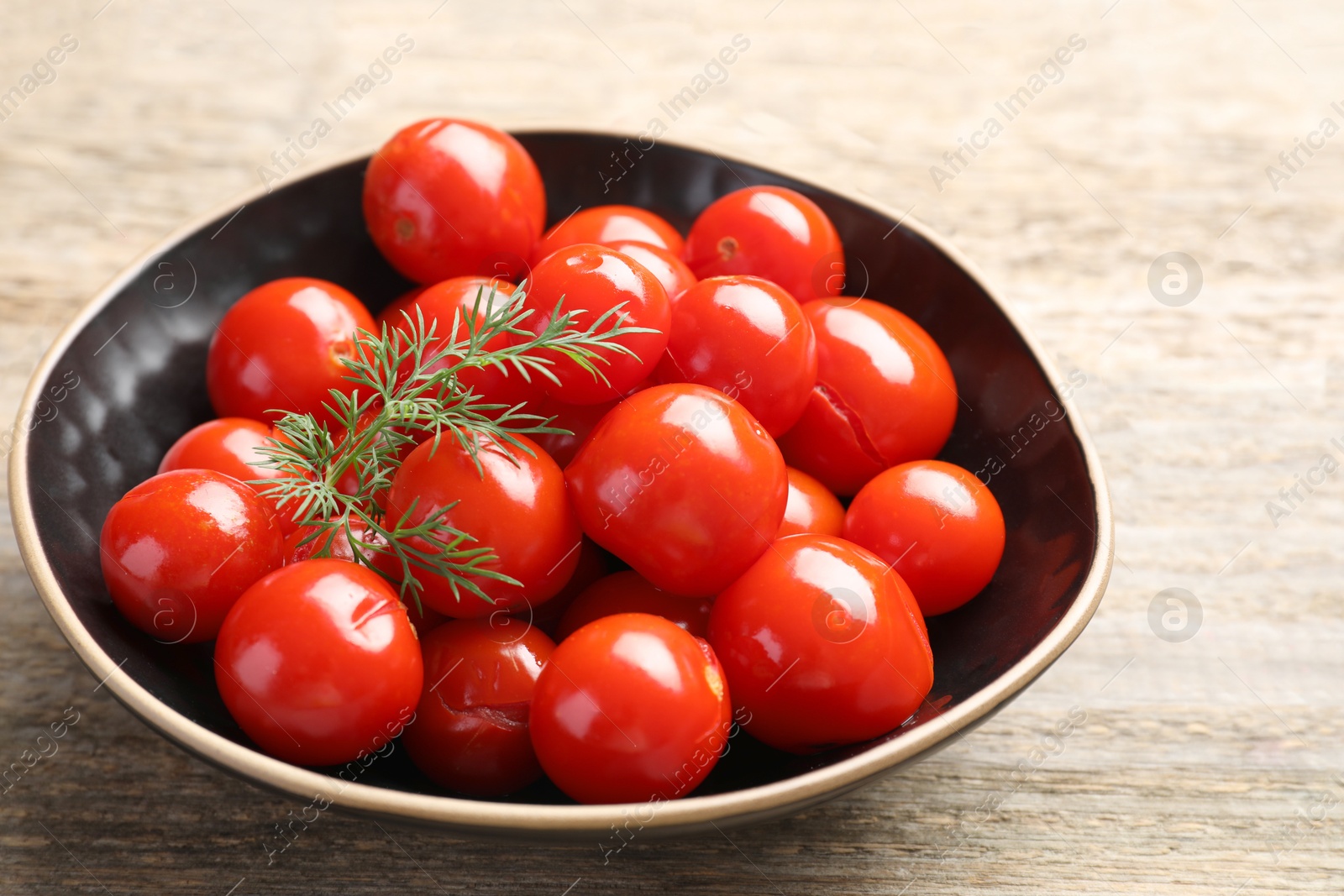 Photo of Tasty pickled tomatoes and dill in bowl on wooden table, closeup