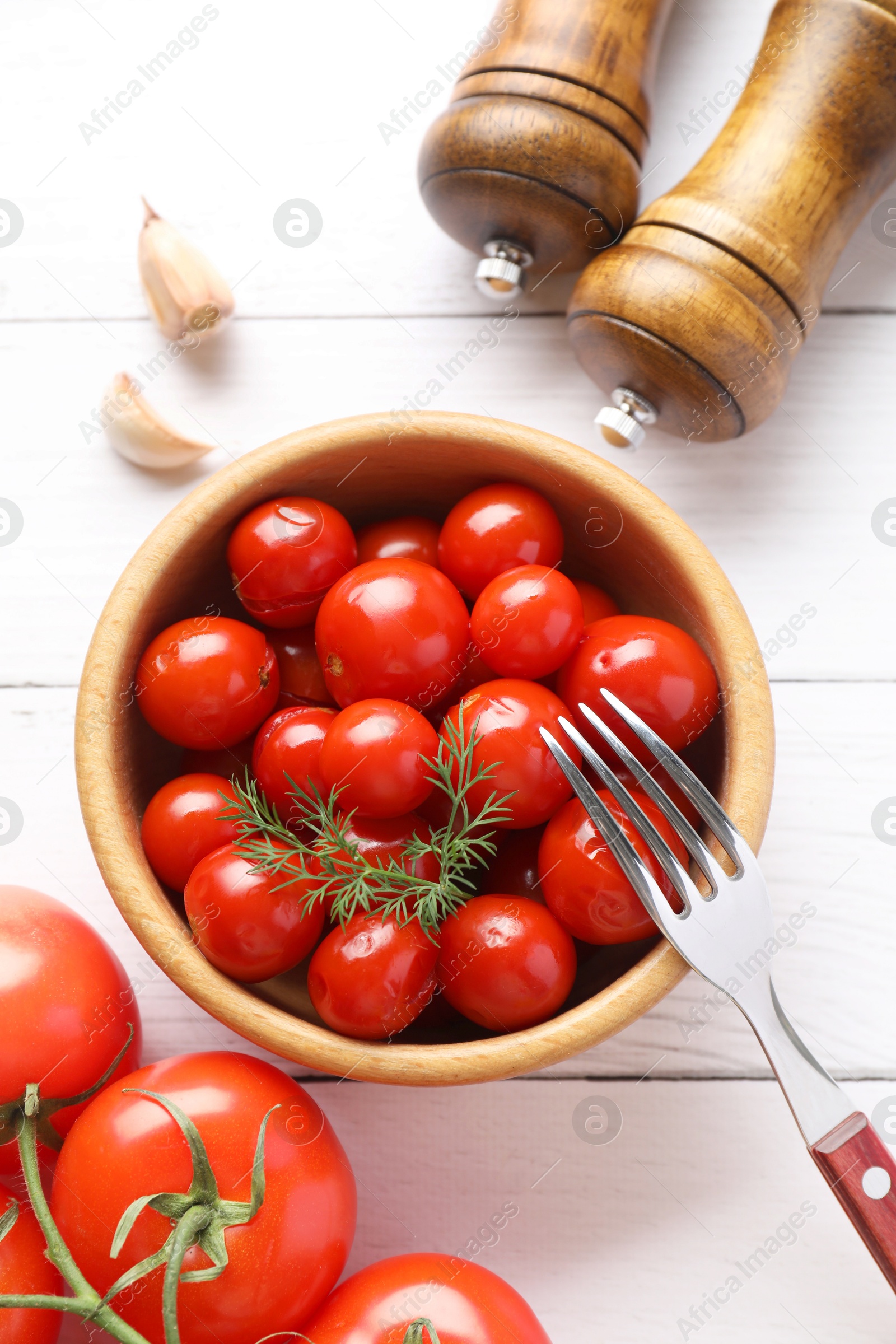 Photo of Tasty pickled tomatoes in bowl, fresh vegetables, dill, garlic and fork on white wooden table, top view