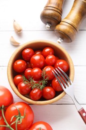 Tasty pickled tomatoes in bowl, fresh vegetables, dill, garlic and fork on white wooden table, top view