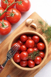 Tasty pickled tomatoes in bowl, fresh vegetables, dill, garlic and fork on white table, top view