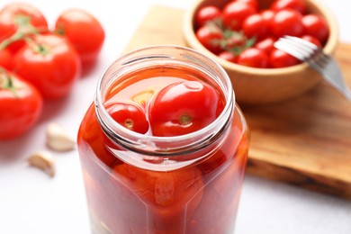 Photo of Tasty pickled tomatoes in jar on white table, closeup