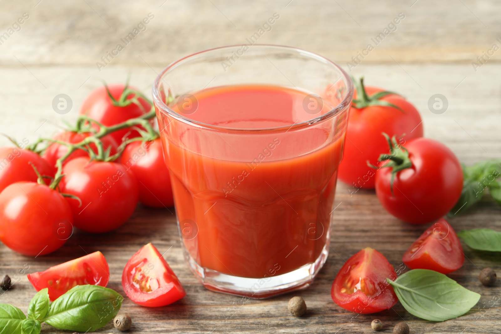 Photo of Tasty tomato juice in glass with fresh vegetables and spices on wooden table, closeup