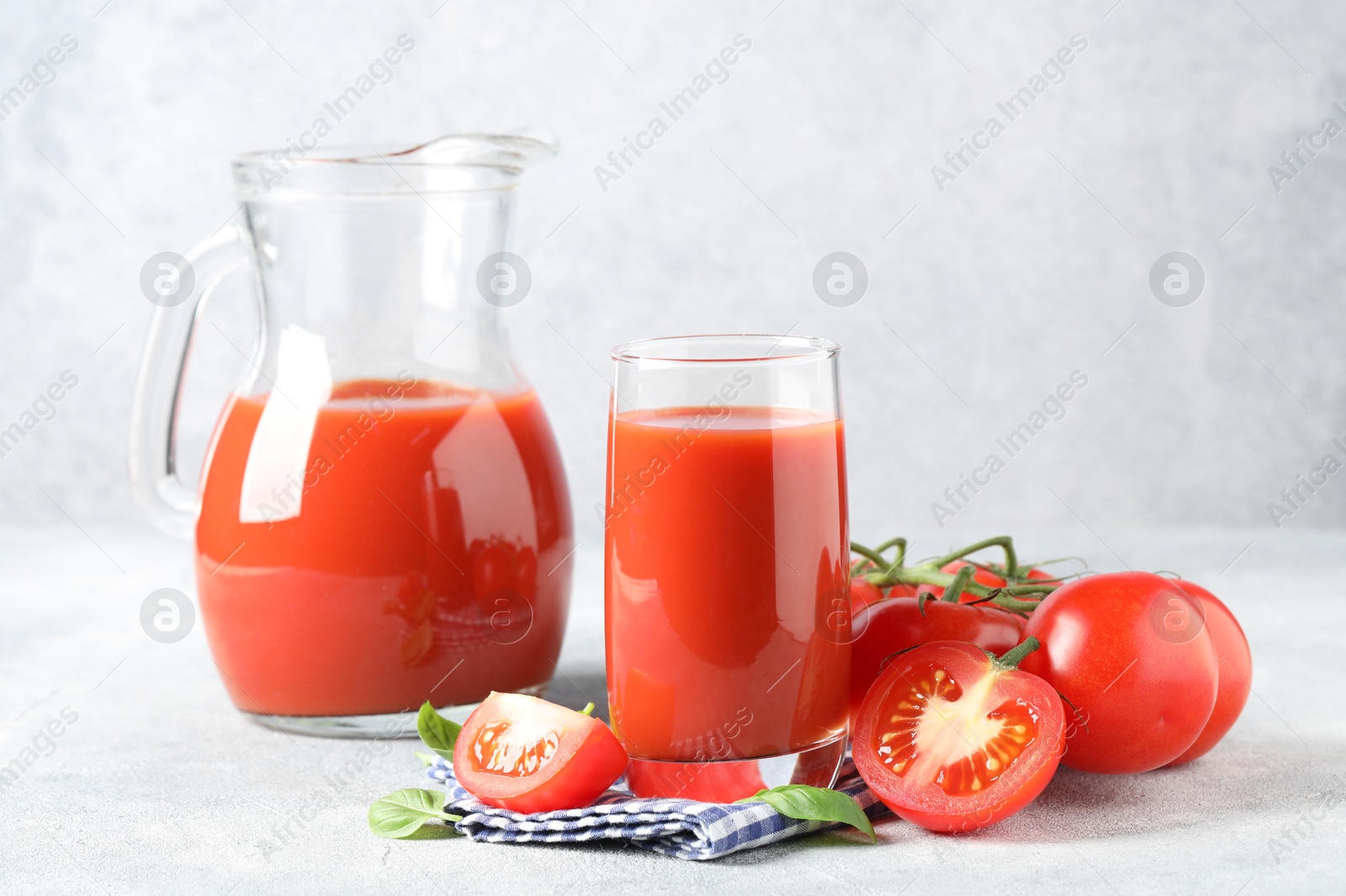 Photo of Tasty tomato juice with fresh vegetables and basil leaves on light grey table