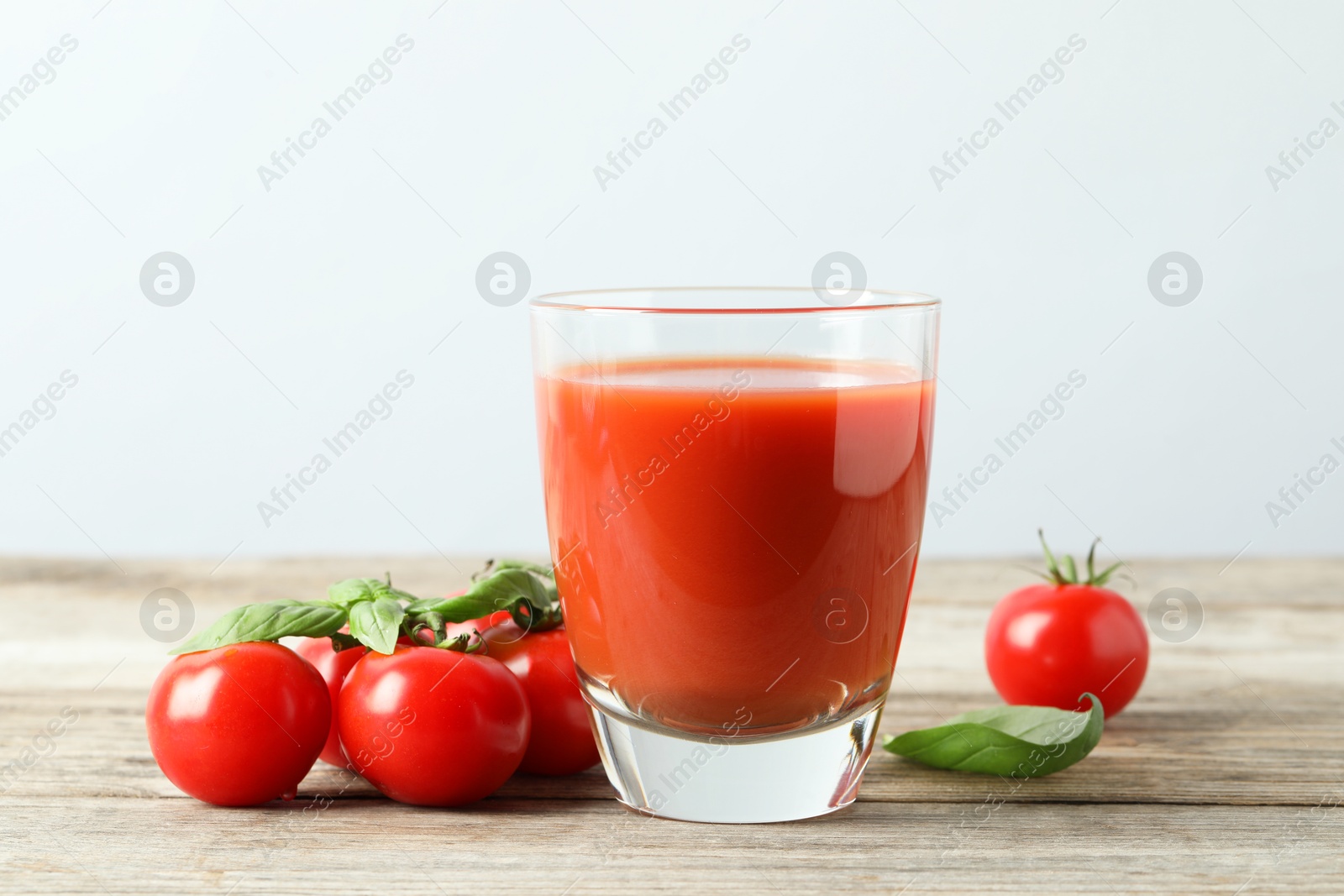 Photo of Tasty tomato juice in glass, basil leaves and fresh vegetables on wooden table