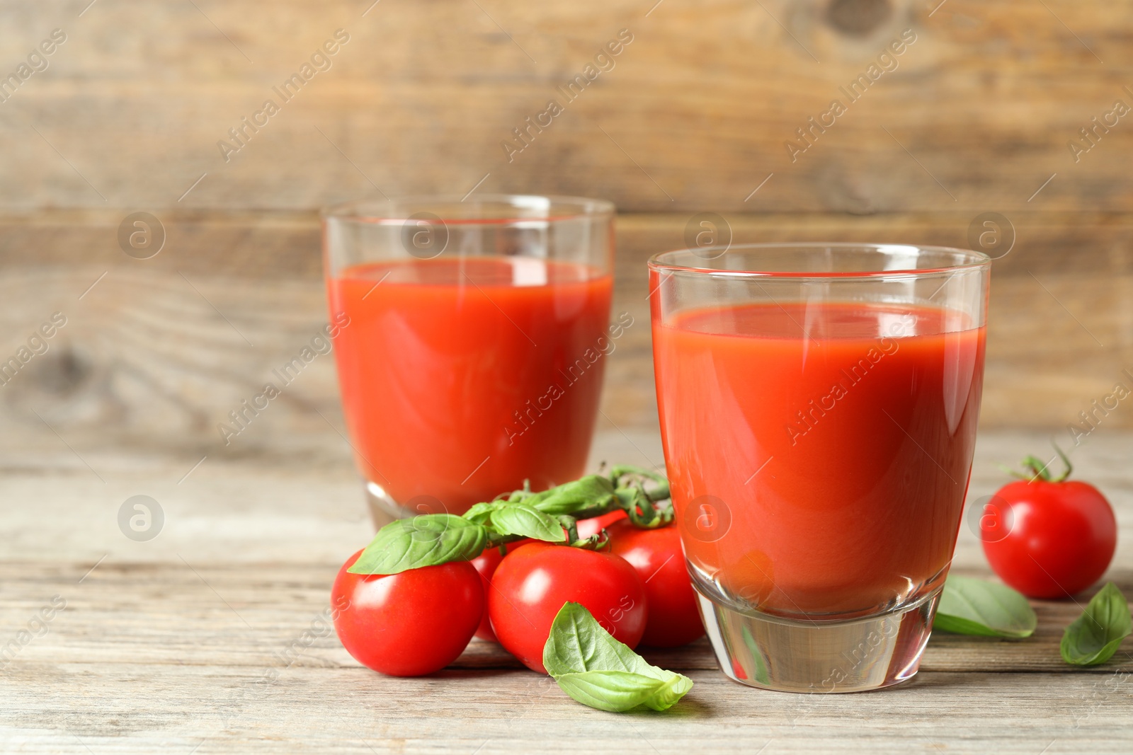 Photo of Tasty tomato juice in glasses, basil leaves and fresh vegetables on wooden table, closeup