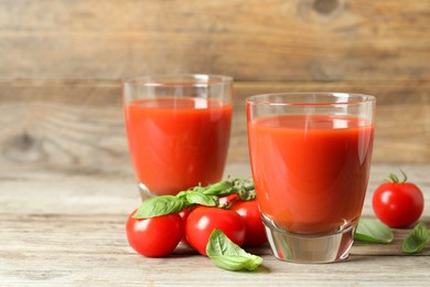 Photo of Tasty tomato juice in glasses, basil leaves and fresh vegetables on wooden table, closeup