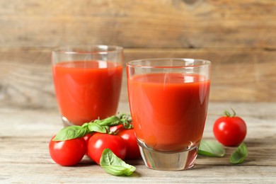 Photo of Tasty tomato juice in glasses, basil leaves and fresh vegetables on wooden table, closeup