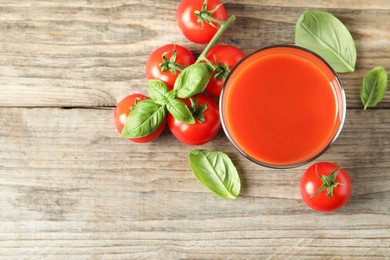 Tasty tomato juice in glass, basil leaves and fresh vegetables on wooden table, flat lay. Space for text