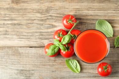 Photo of Tasty tomato juice in glass, basil leaves and fresh vegetables on wooden table, flat lay. Space for text