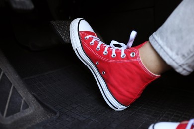 Photo of Woman in sneakers pushing on pedal of car brake, closeup