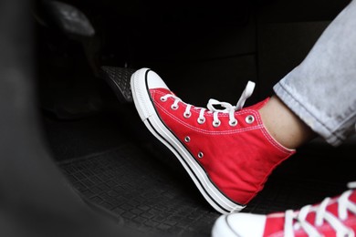 Woman in sneakers pushing on pedal of car brake, closeup