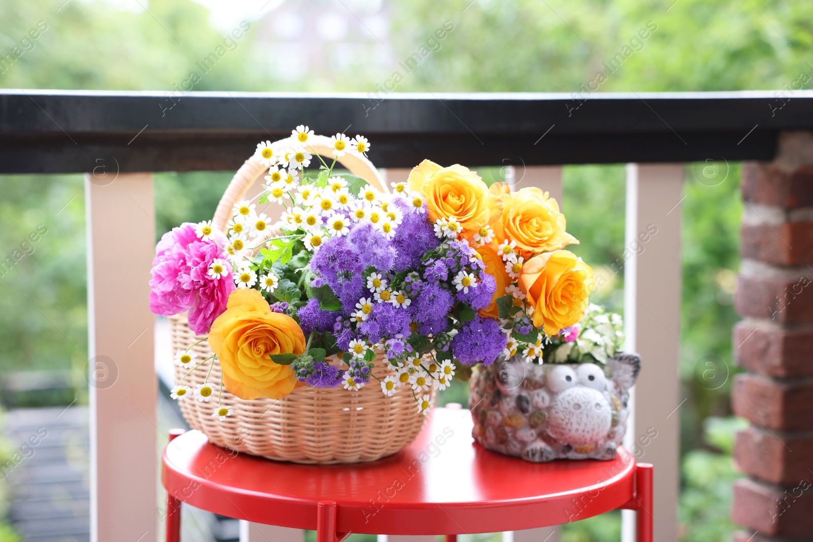 Photo of Wicker basket with beautiful flowers on red table at balcony