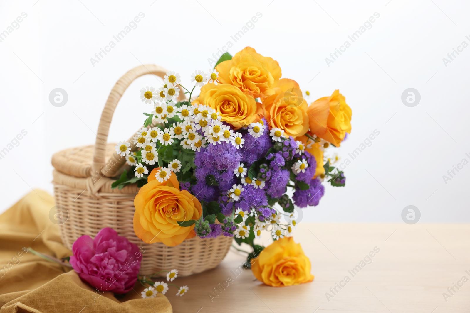 Photo of Wicker basket with beautiful flowers on light wooden table, space for text