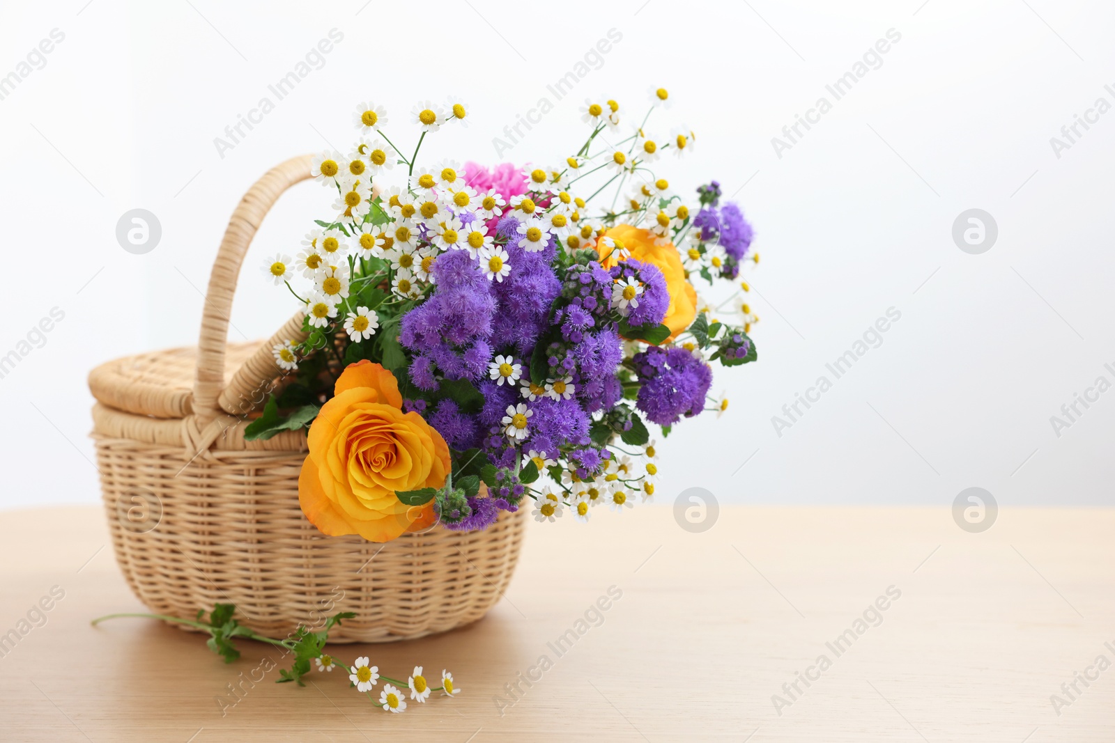 Photo of Wicker basket with beautiful flowers on light wooden table, space for text