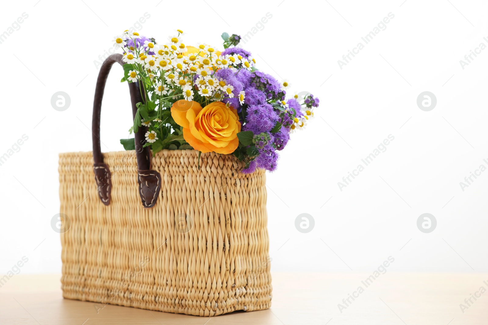 Photo of Wicker basket with beautiful flowers on light wooden table, space for text