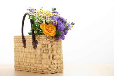 Photo of Wicker basket with beautiful flowers on light wooden table, space for text