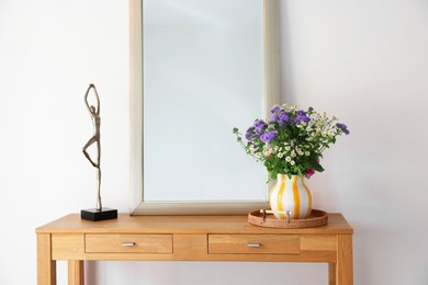 Photo of Beautiful flowers in vase and mirror on wooden table indoors