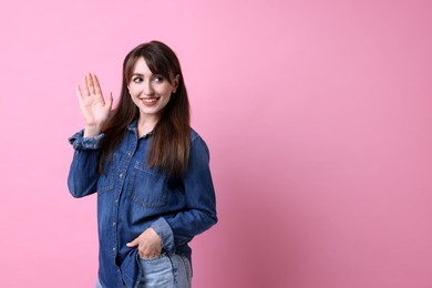 Photo of Happy young woman waving on pink background, space for text
