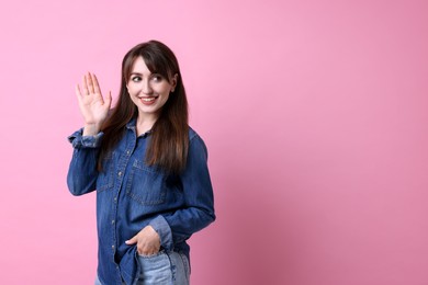 Happy young woman waving on pink background, space for text