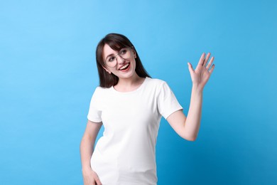 Photo of Happy woman waving on light blue background