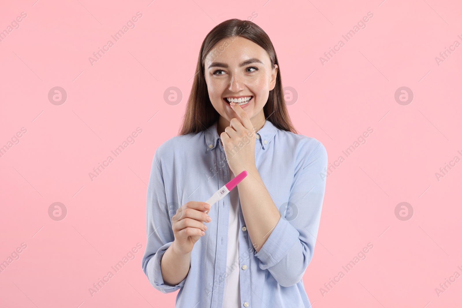 Photo of Happy woman holding pregnancy test on pink background