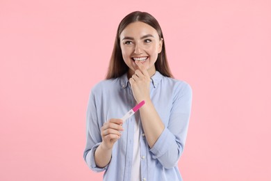 Happy woman holding pregnancy test on pink background