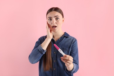 Shocked woman holding pregnancy test on pink background