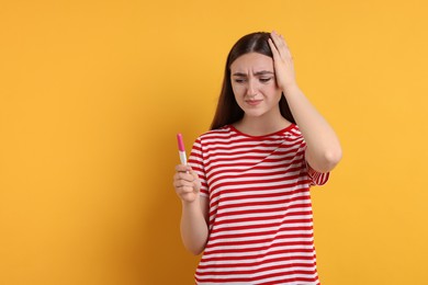 Confused woman holding pregnancy test on orange background, space for text