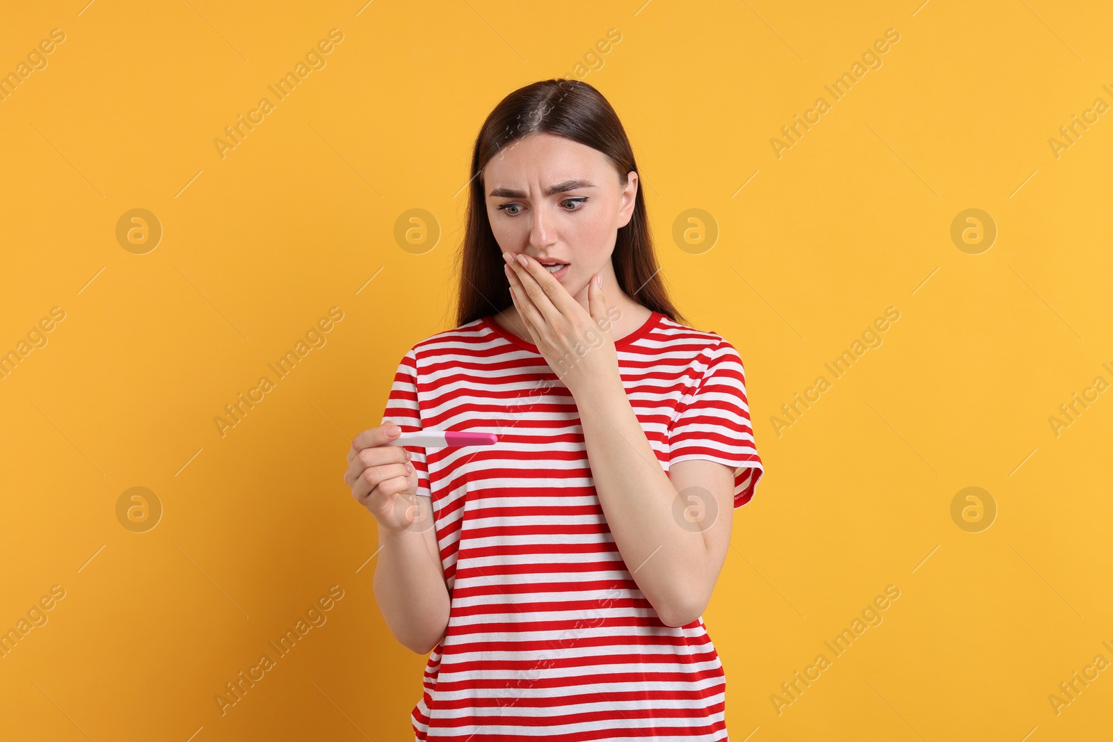 Photo of Shocked woman holding pregnancy test on orange background