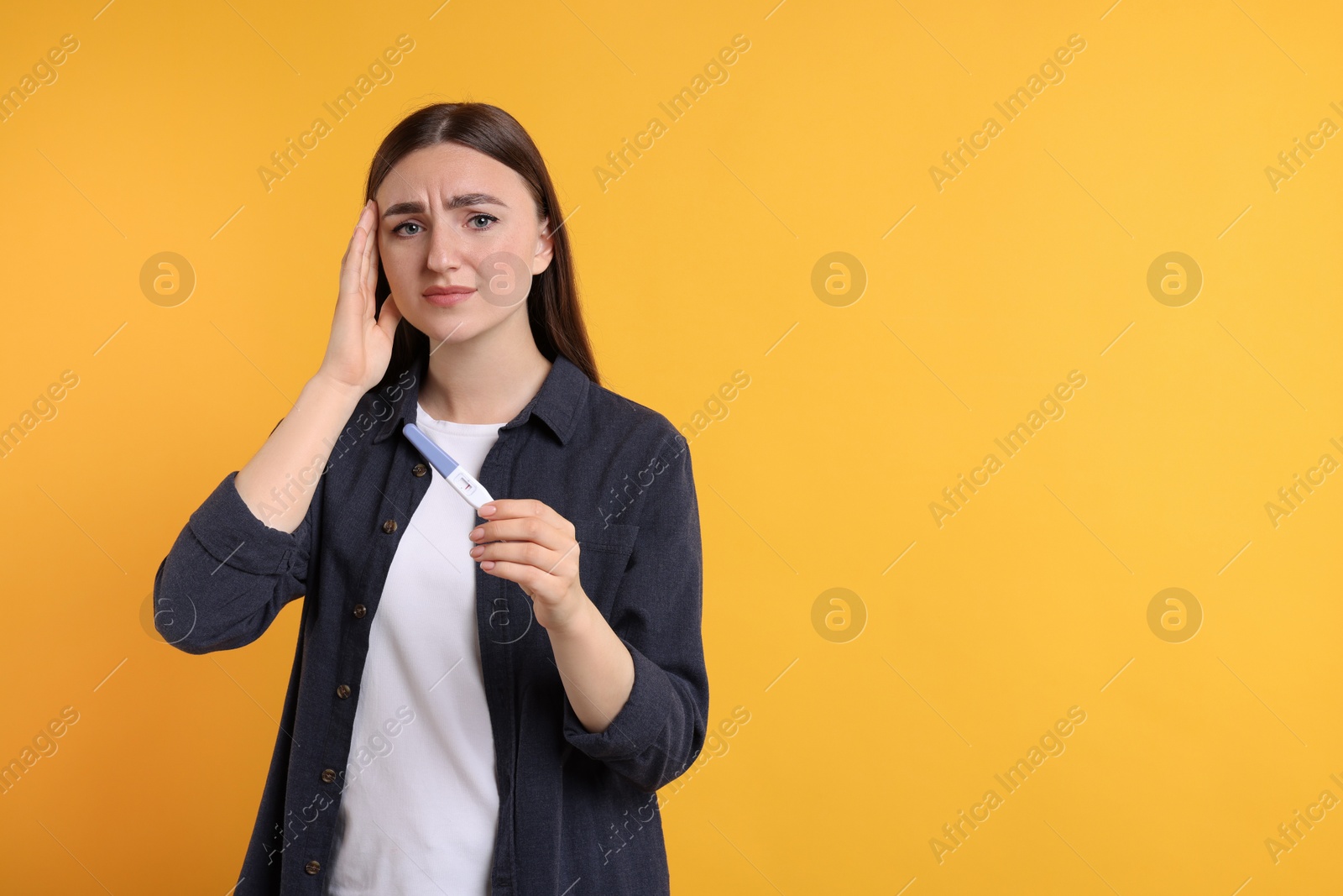 Photo of Sad woman holding pregnancy test on orange background, space for text