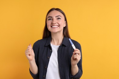 Photo of Happy woman holding pregnancy test on orange background