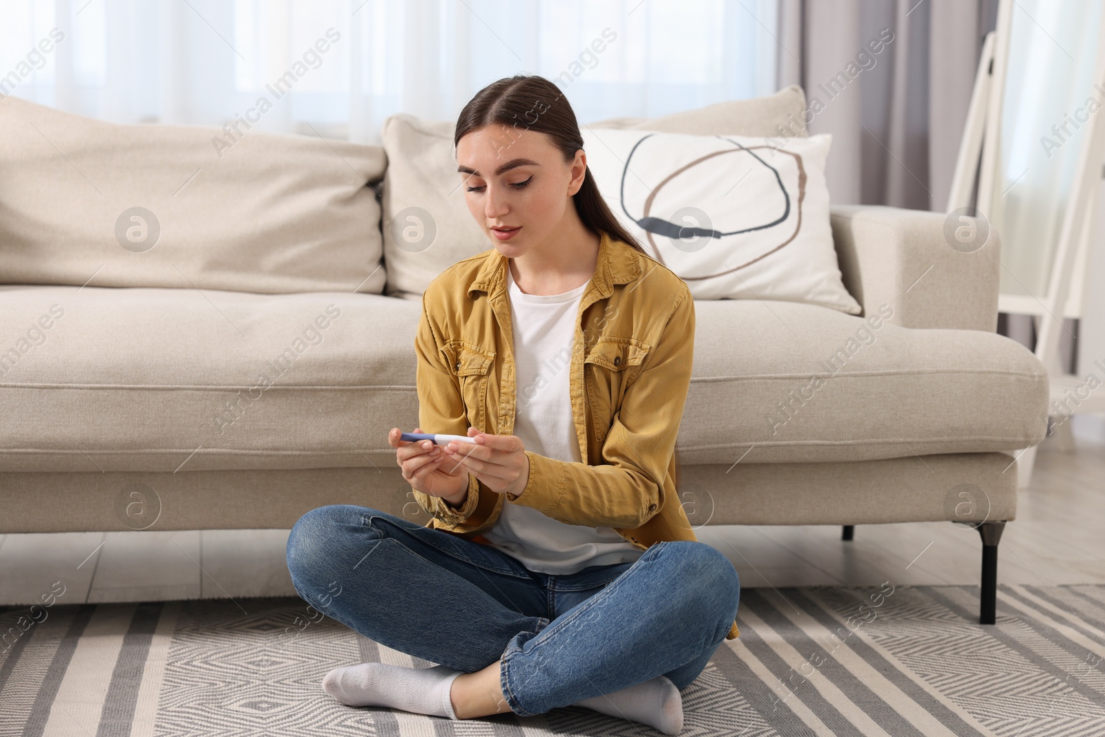 Photo of Woman holding pregnancy test on floor indoors