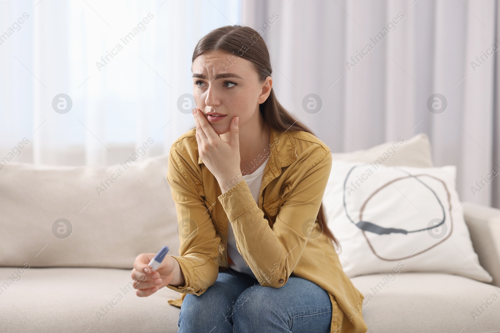 Photo of Sad woman holding pregnancy test on sofa indoors