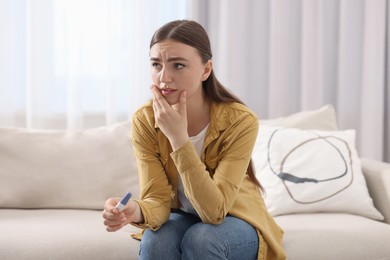 Photo of Sad woman holding pregnancy test on sofa indoors
