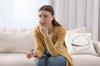 Sad woman holding pregnancy test on sofa indoors