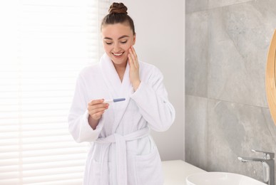 Photo of Happy woman holding pregnancy test in bathroom