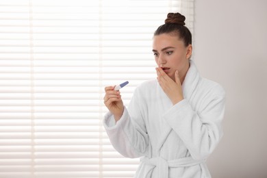 Photo of Shocked woman holding pregnancy test in bathroom, space for text