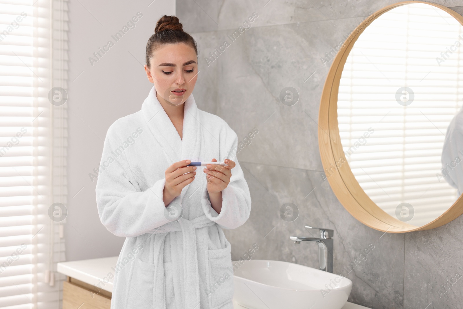 Photo of Sad woman holding pregnancy test in bathroom