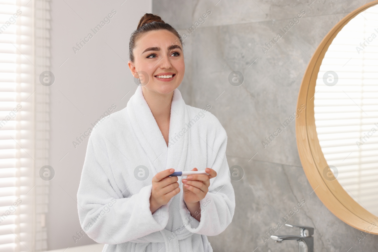 Photo of Happy woman holding pregnancy test in bathroom