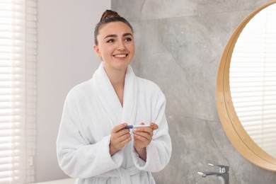 Happy woman holding pregnancy test in bathroom