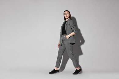 Beautiful woman in stylish suit walking on gray background