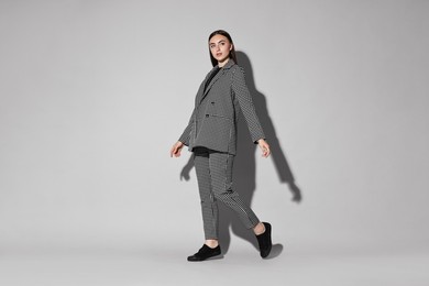 Photo of Beautiful woman in stylish suit walking on gray background