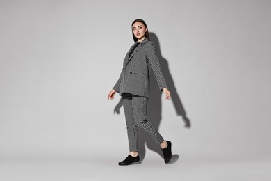 Beautiful woman in stylish suit walking on gray background