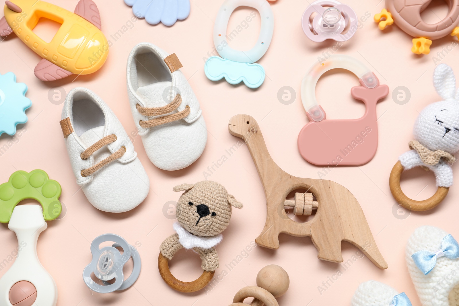 Photo of Colorful rattles, baby shoes and pacifiers on beige background, flat lay