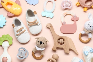 Colorful rattles, baby shoes and pacifiers on beige background, flat lay