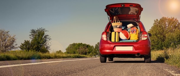 Family car with open trunk full of luggage on highway. Banner design with space for text